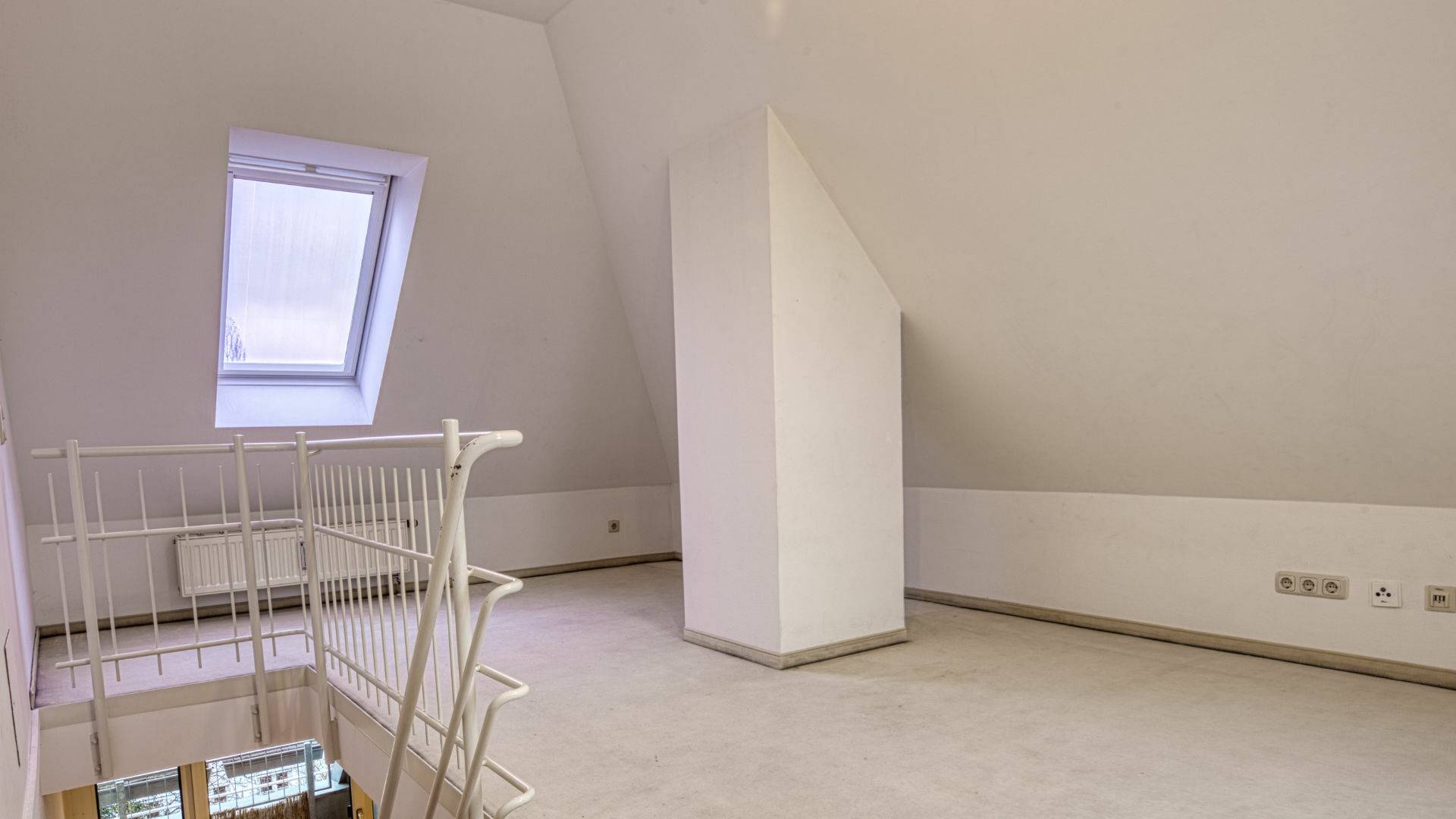 Leerer Raum mit Dachschräge, Dachfenster und Geländer in einer Dachgeschosswohnung in München-Thalkirchen