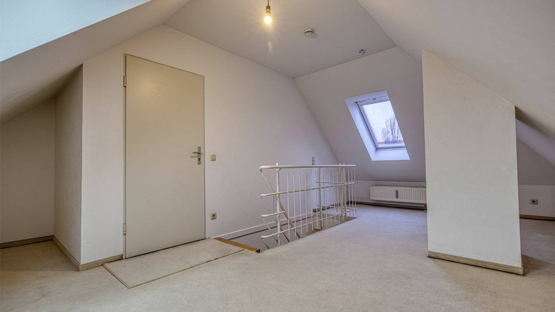 Leerer Raum mit Dachschräge, Dachfenster und Geländer zum Treppenaufgang in einer Wohnung in München-Thalkirchen