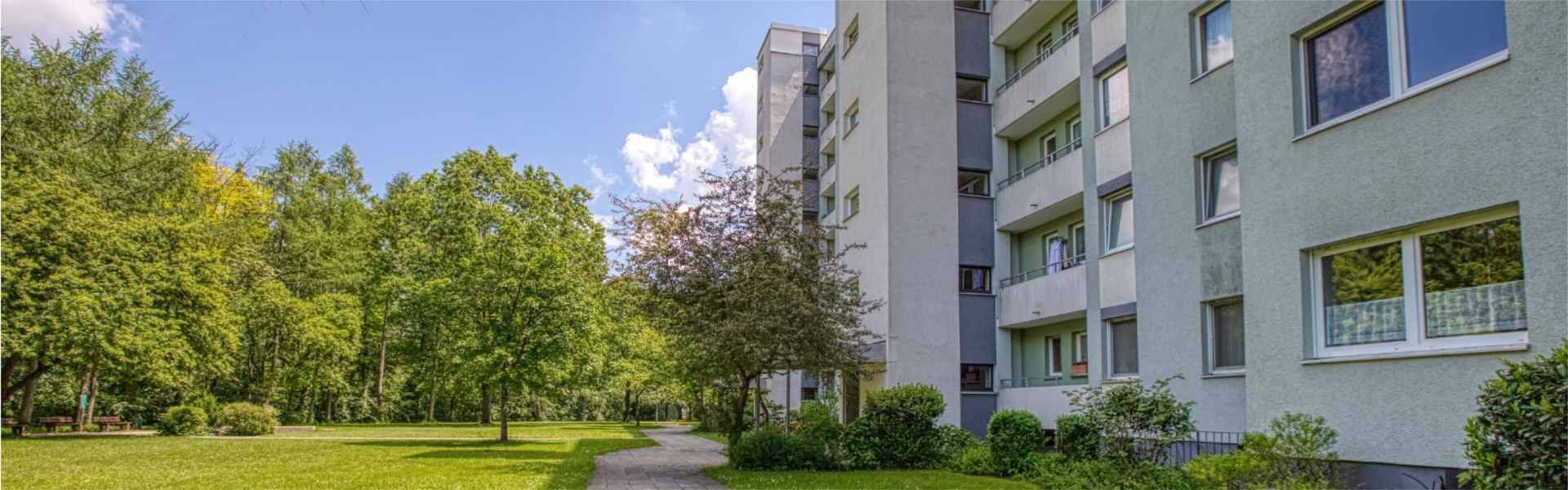 Panoramaansicht eines Wohnhauses mit begrüntem Vorplatz, Bäumen und Weg in Unterhaching.