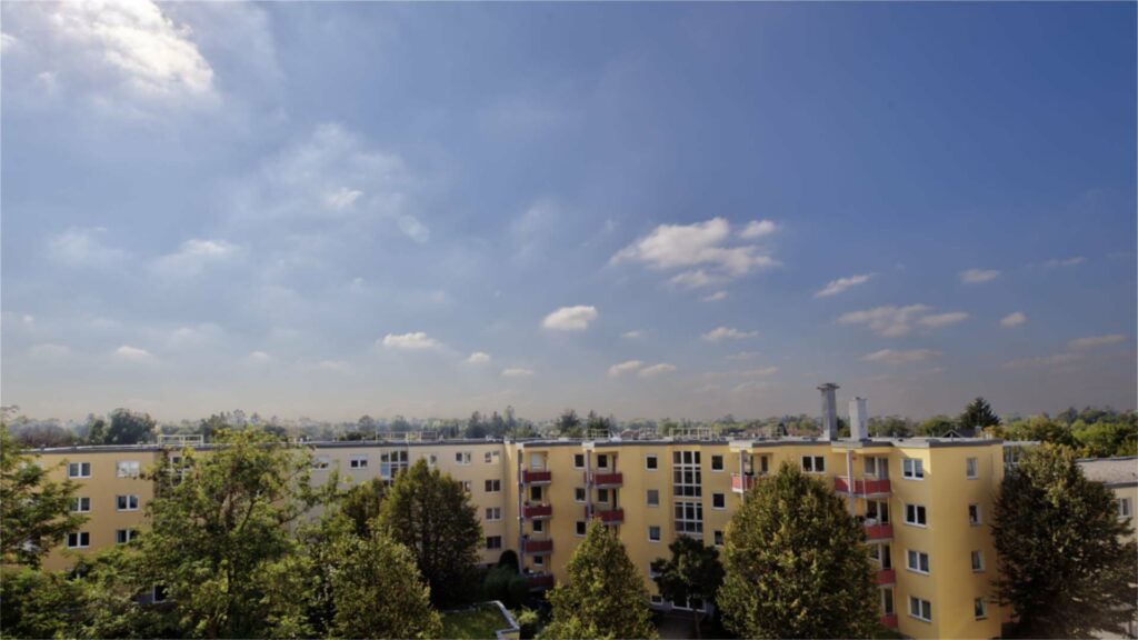 Far-reaching view over yellow apartment blocks and trees from a high floor in Munich-Untermenzing.
