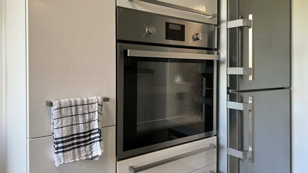 Built-in oven with control panel next to refrigerator and tea towel in the kitchen of an apartment in Munich-Untermenzing