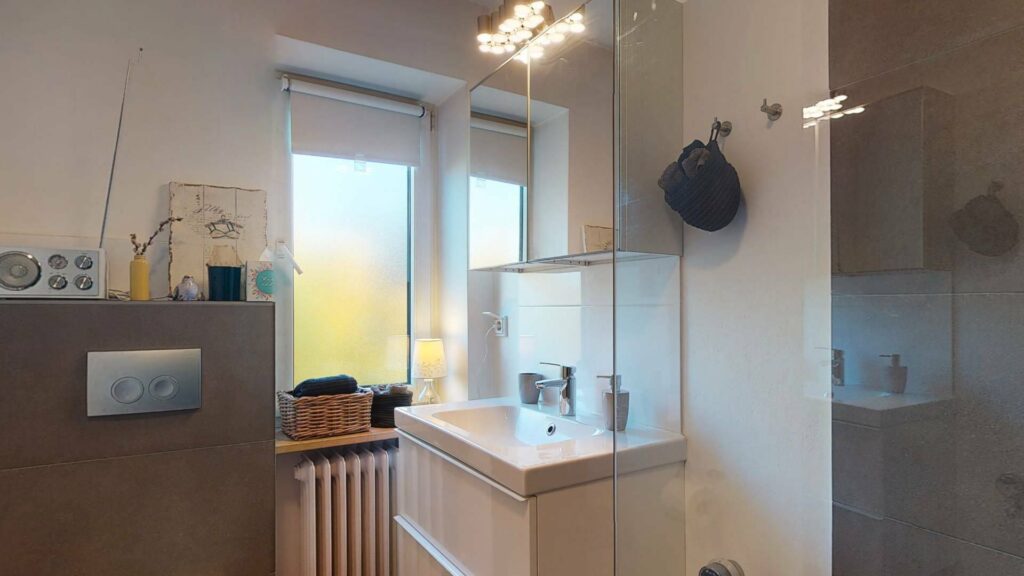 Bathroom with glass shower, sink, and window in a condominium in Untermenzing.