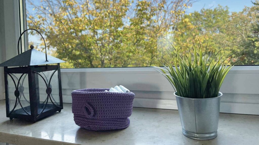 Windowsill with lantern, small basket, and artificial plant in front of autumn leaves in an apartment in Untermenzing.