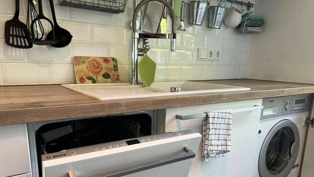 Kitchenette with sink, faucet, cutting board, and washing machine underneath in an apartment in Munich-Untermenzing