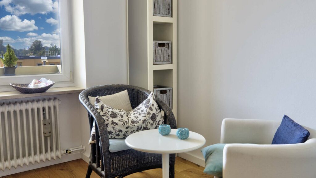 Cozy sitting area with rattan chair, pillows and side table by the window in an apartment in Untermenzing.