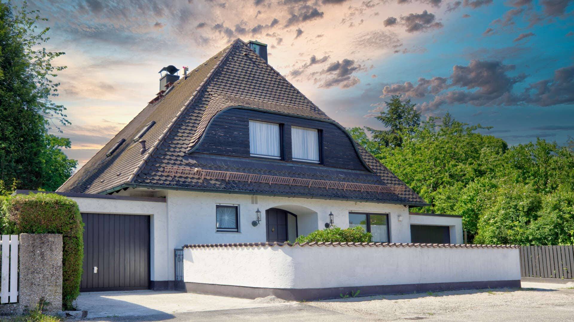 Weißer Bungalow mit dunklem Walmdach vor dramatischem Abendhimmel