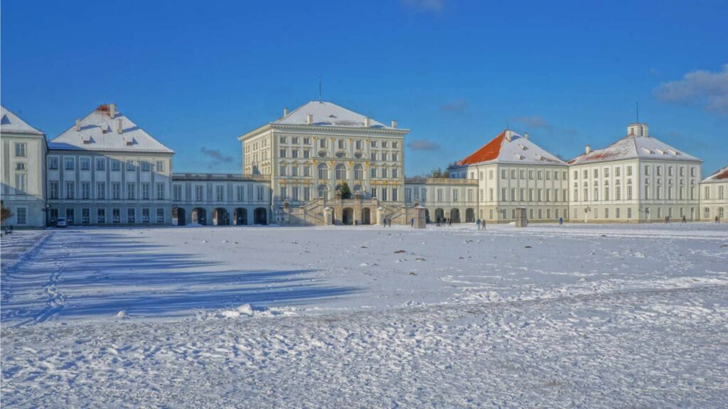 Historisches Schlossgebäude in München mit verschneiter Grünfläche und blauem Himmel – Symbolbild zum Wintercheck fürs Haus