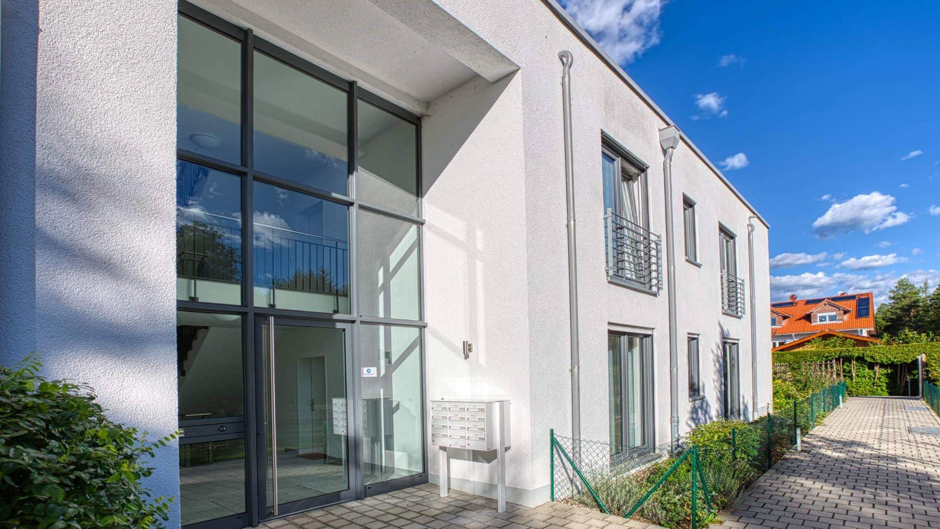 Modern house facade with large glass front, terrace, and paved driveway in Wolfratshausen