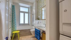 Bathroom of the old apartment in the Au with a bathtub, patterned curtain, and yellow stool