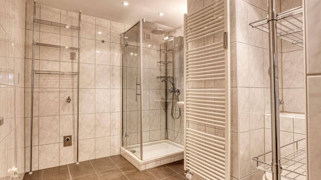 Badezimmer in Aubing mit begehbarer Glasdusche, Handtuchheizkörper und hellen Fliesen.