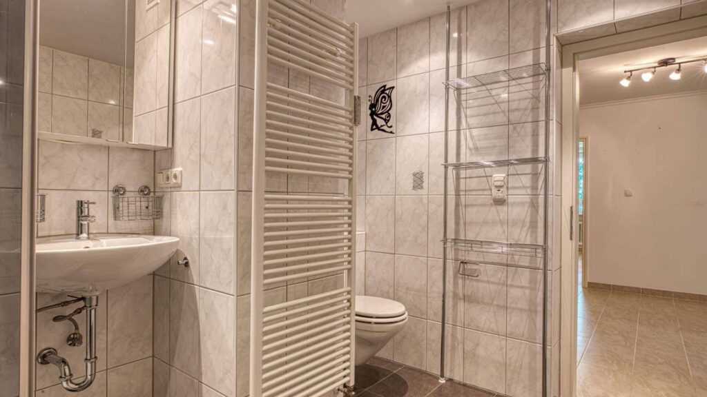 Badezimmer der Wohnung in Aubing mit Waschbecken, WC, Raumteiler und gefliestem Boden, Blick zum Flur