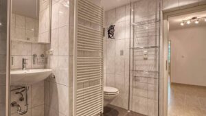 Bathroom in the apartment in Aubing with sink, toilet, partition and tiled floor, view to the hallway