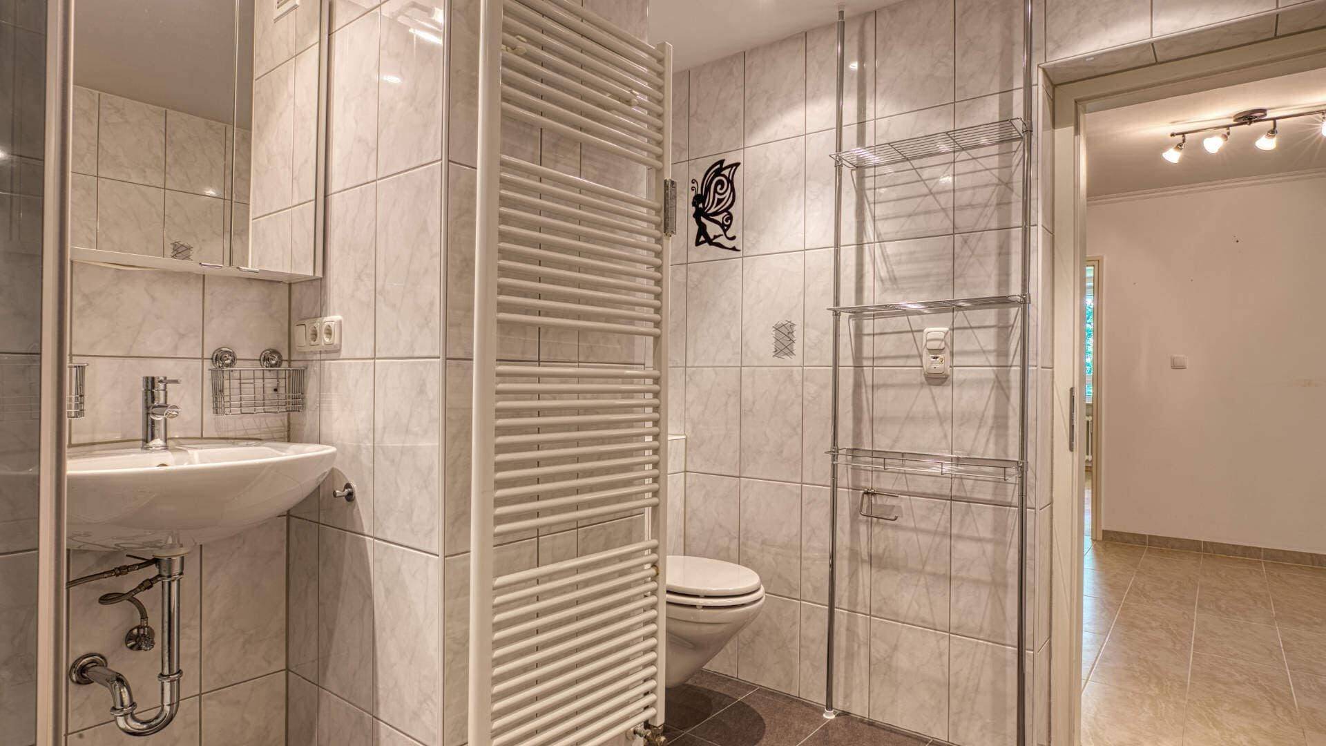 Bathroom in the apartment in Aubing with sink, toilet, partition and tiled floor, view to the hallway