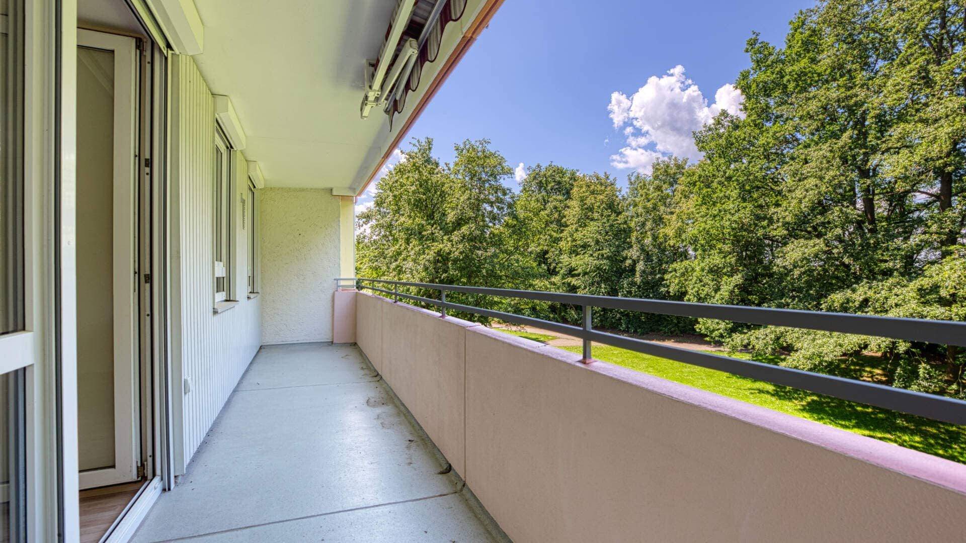 Long balcony of an apartment in Aubing with a view of trees and blue sky.