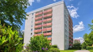 Exterior view of the residential high-rise building in Aubing with red-orange balconies surrounded by green spaces and a blue sky