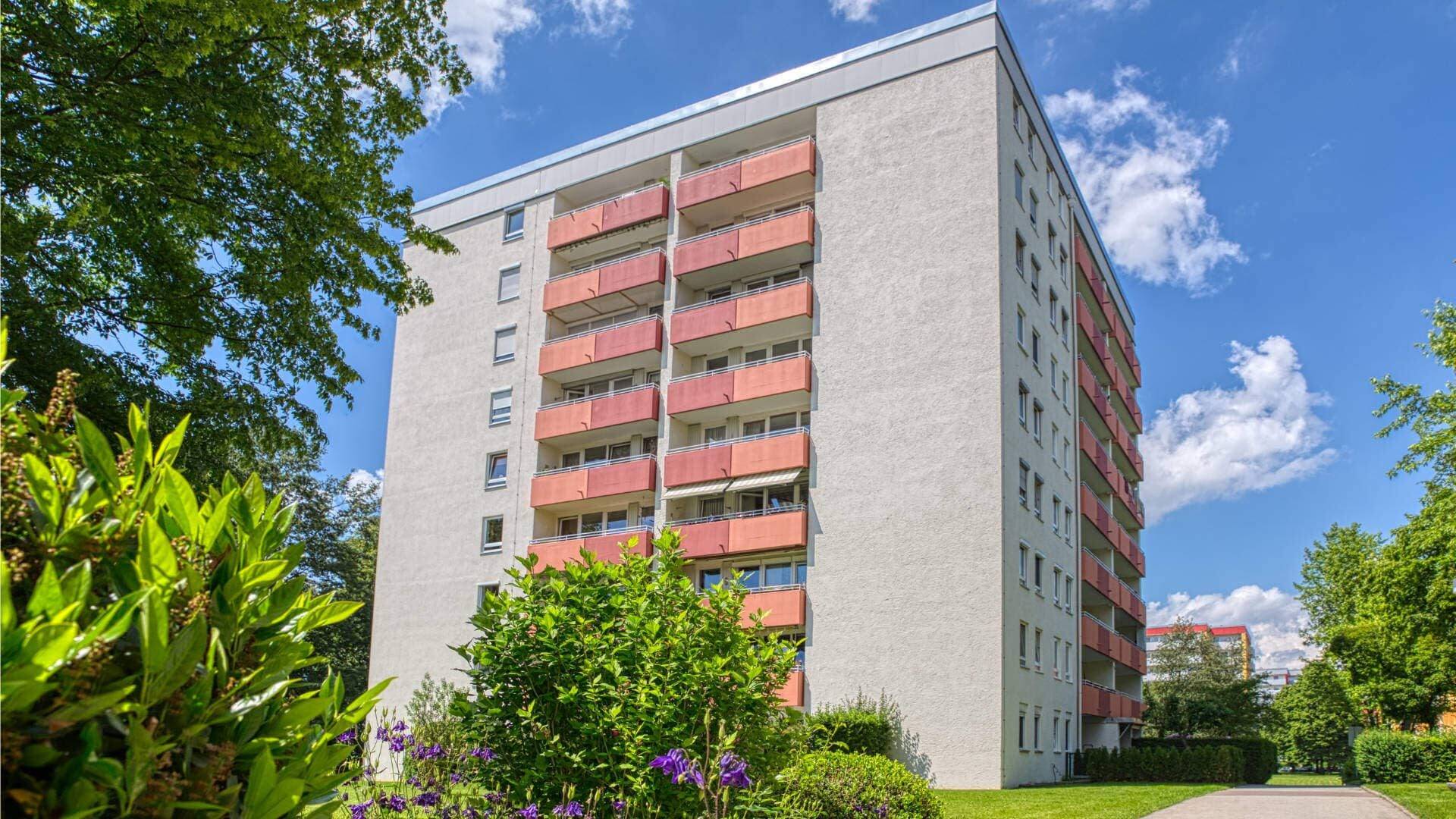 Exterior view of the residential high-rise building in Aubing with red-orange balconies surrounded by green spaces and a blue sky