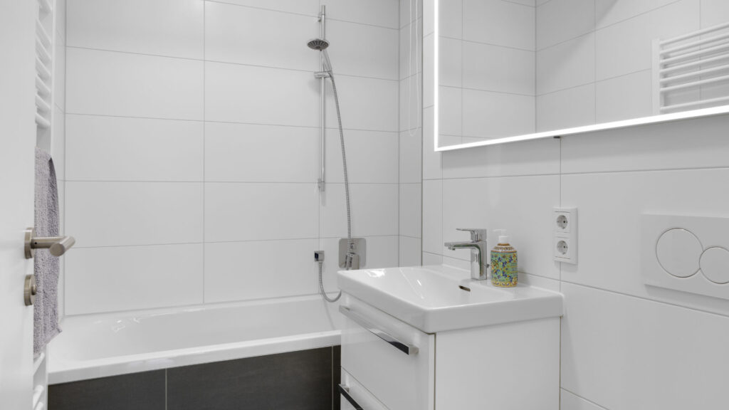 Compact bathroom with a bathtub and illuminated mirror in an apartment in Munich-Aubing