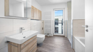 Bathroom of the new-build apartment in Aubing with washbasin, towel radiator, and access to the balcony