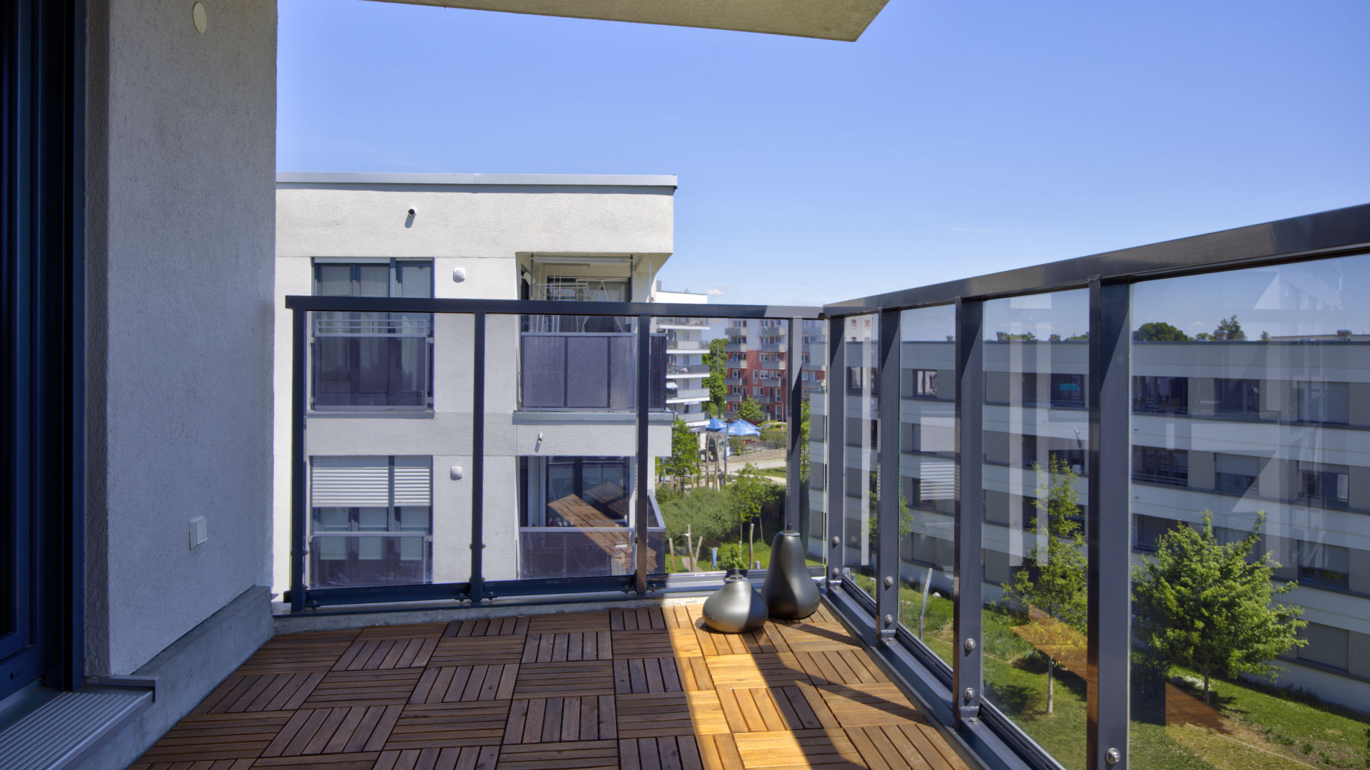 Balcony of the new apartment in Aubing with wooden plank flooring, glass railing, and a view over the courtyard
