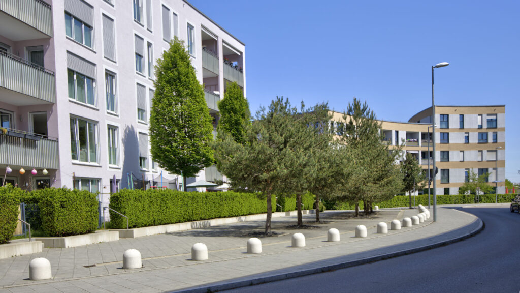 Facade of a multi-story residential building with hedges and a street in Munich-Aubing