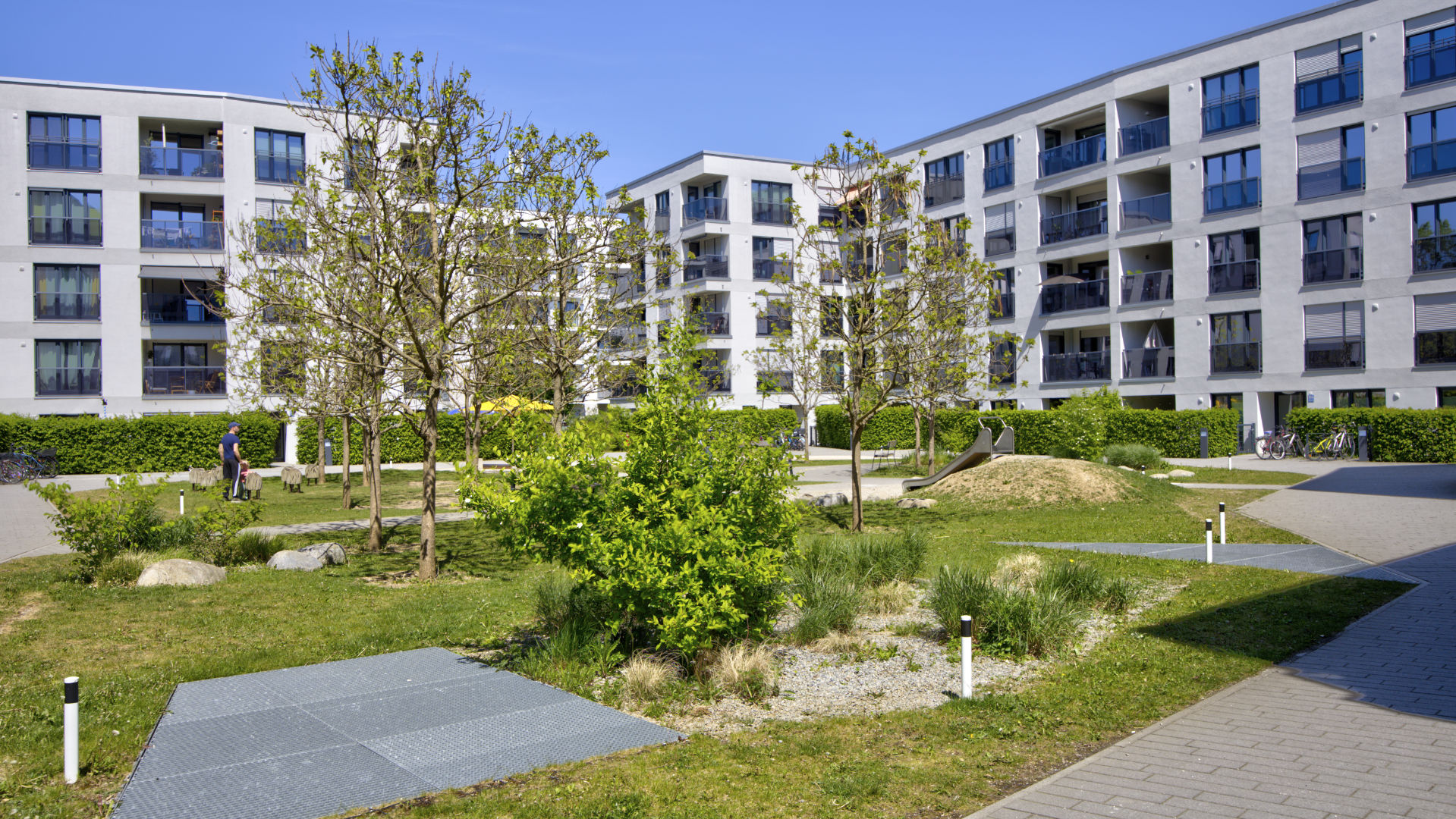 Spacious green area of the Aubing residential complex with trees, paths, and play hill between the buildings