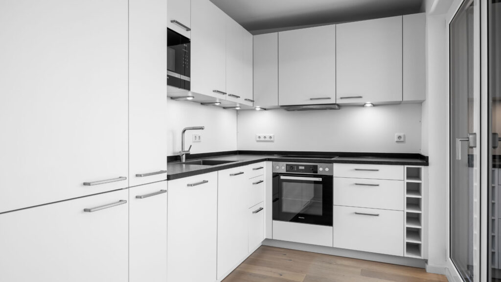 White fitted kitchen in the Aubing new-build apartment with a black countertop, oven, and wine rack