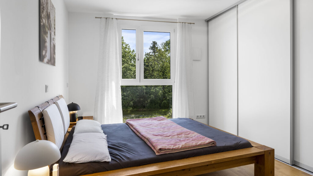 Bedroom with double bed, built-in wardrobe, and window with green view in Aubing apartment