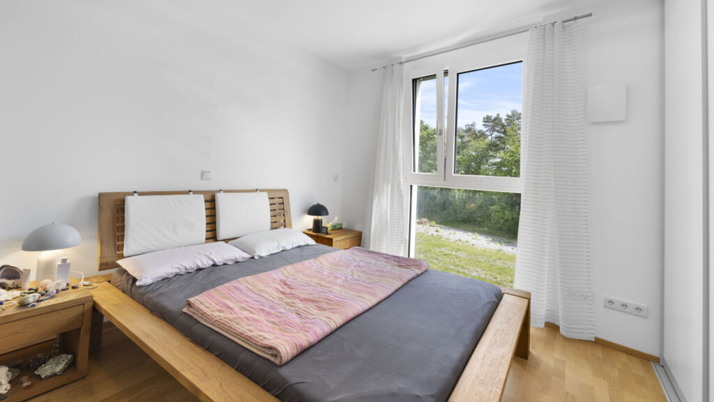 Bedroom with a low double bed and a large window in a condominium in Munich-Aubing