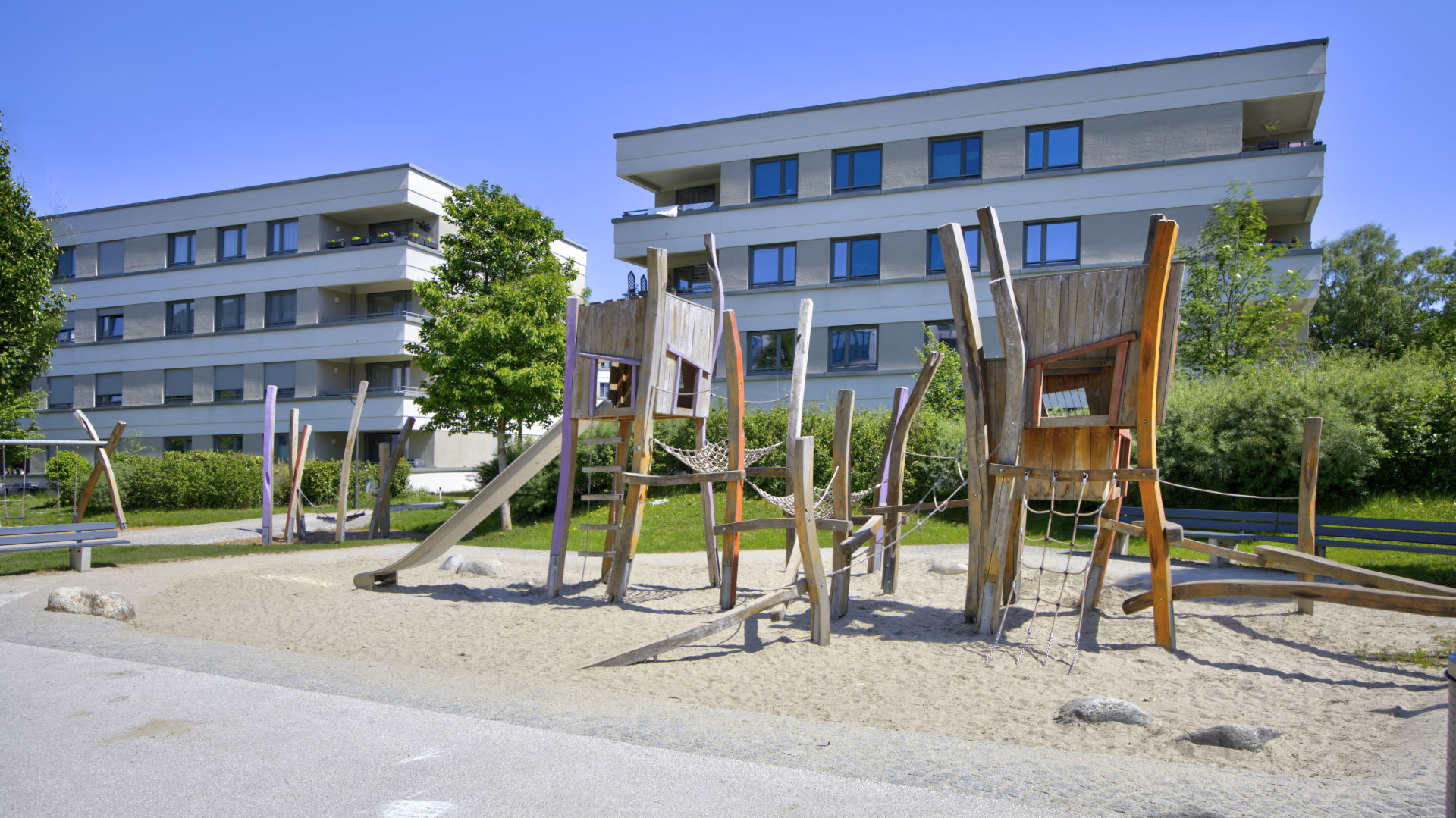 Natural wood play equipment with a slide and climbing net in the sand playground of the Aubing residential complex
