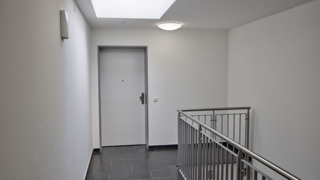 Stairwell of the Aubing residential complex with apartment door, stone floor, and stainless steel railing