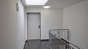 Stairwell of the Aubing residential complex with apartment door, stone floor, and stainless steel railing