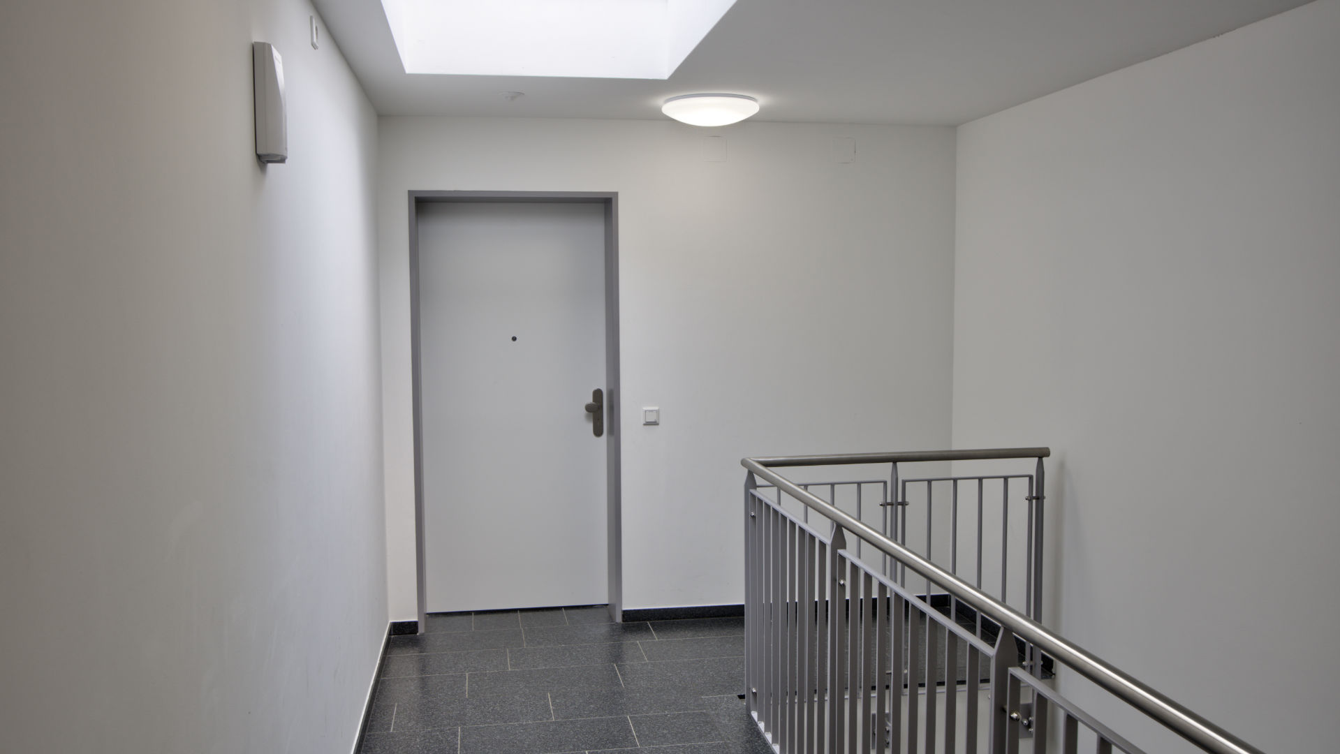 Stairwell of the Aubing residential complex with apartment door, stone floor, and stainless steel railing