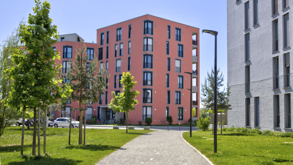 Modern residential complex with a red brick facade and green spaces in the area of an apartment in Munich-Aubing