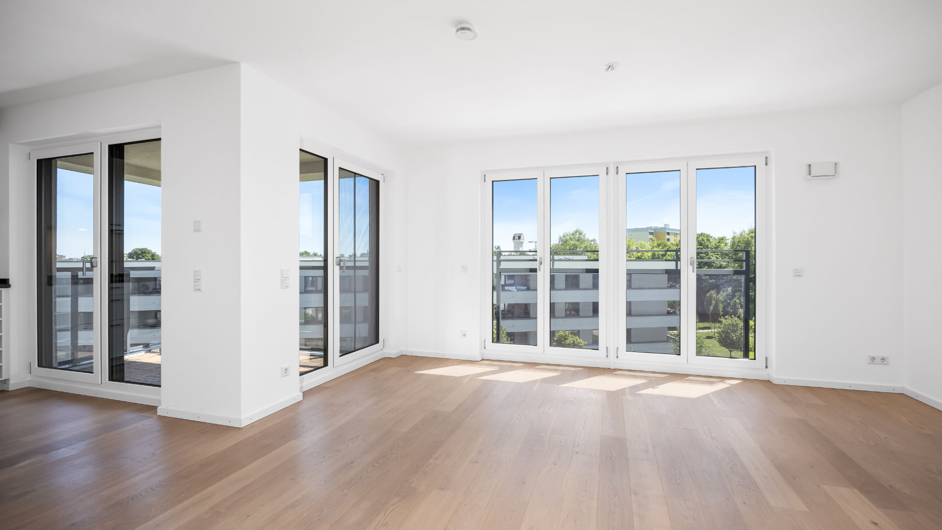 Open-plan living and dining area of the new-build apartment in Aubing with several French doors and parquet flooring