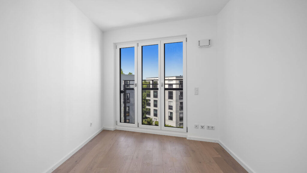 Empty room with balcony door and view of the new development in Munich-Aubing – Rogers Immobilien