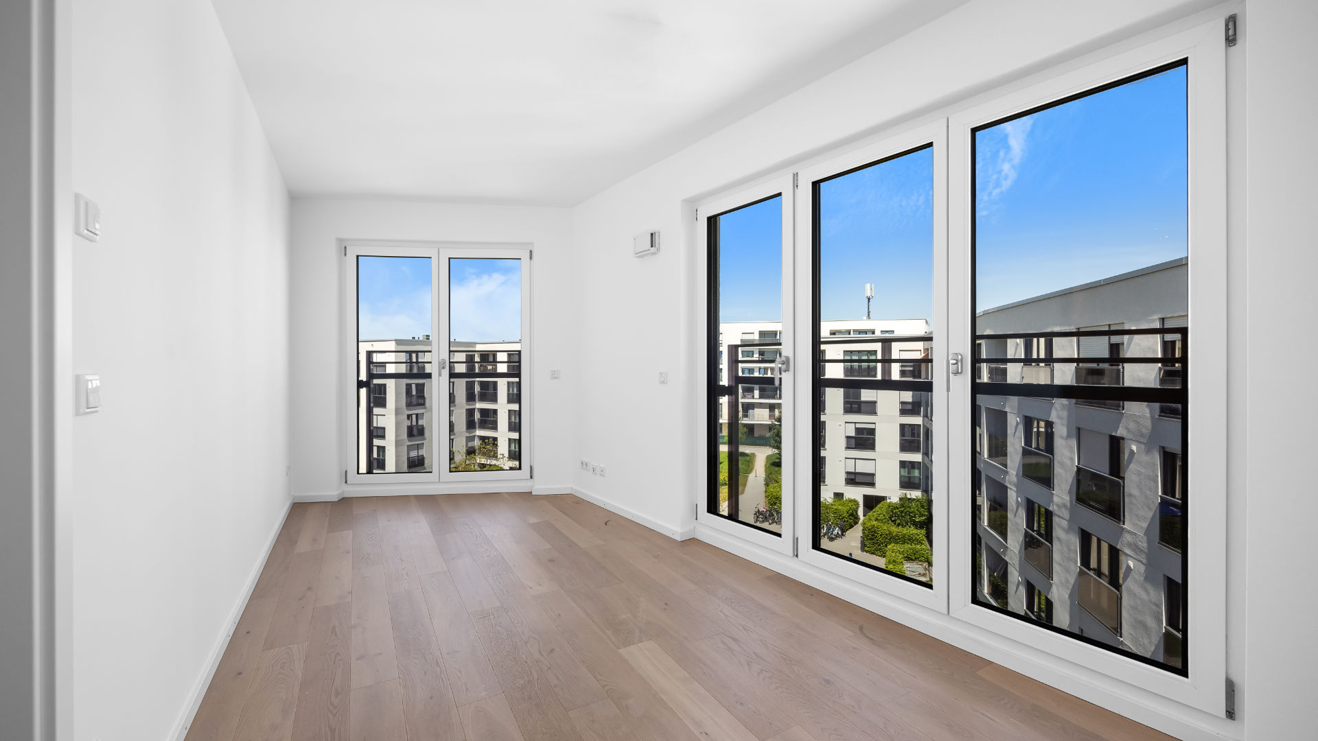 Empty room with a large floor-to-ceiling window and a view of the new Aubing residential development – Rogers Immobilien