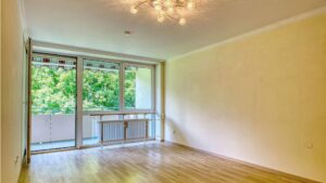 Living room of the apartment in Aubing with chandelier, balcony door, parquet floor and view of trees