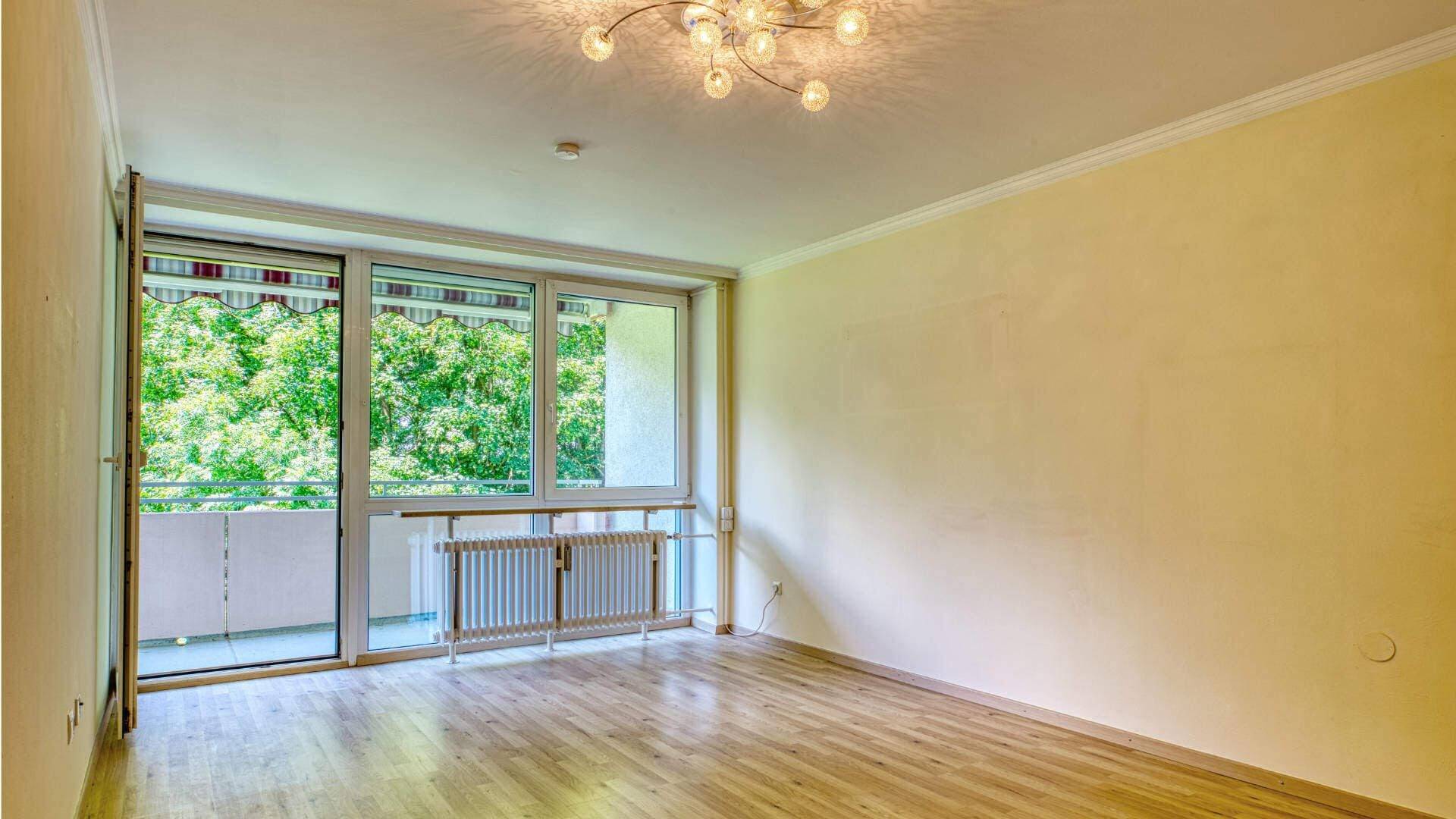 Living room of the apartment in Aubing with chandelier, balcony door, parquet floor and view of trees