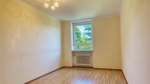 Empty room in the apartment in Aubing with a ceiling light, windows, radiators, and a light wooden floor