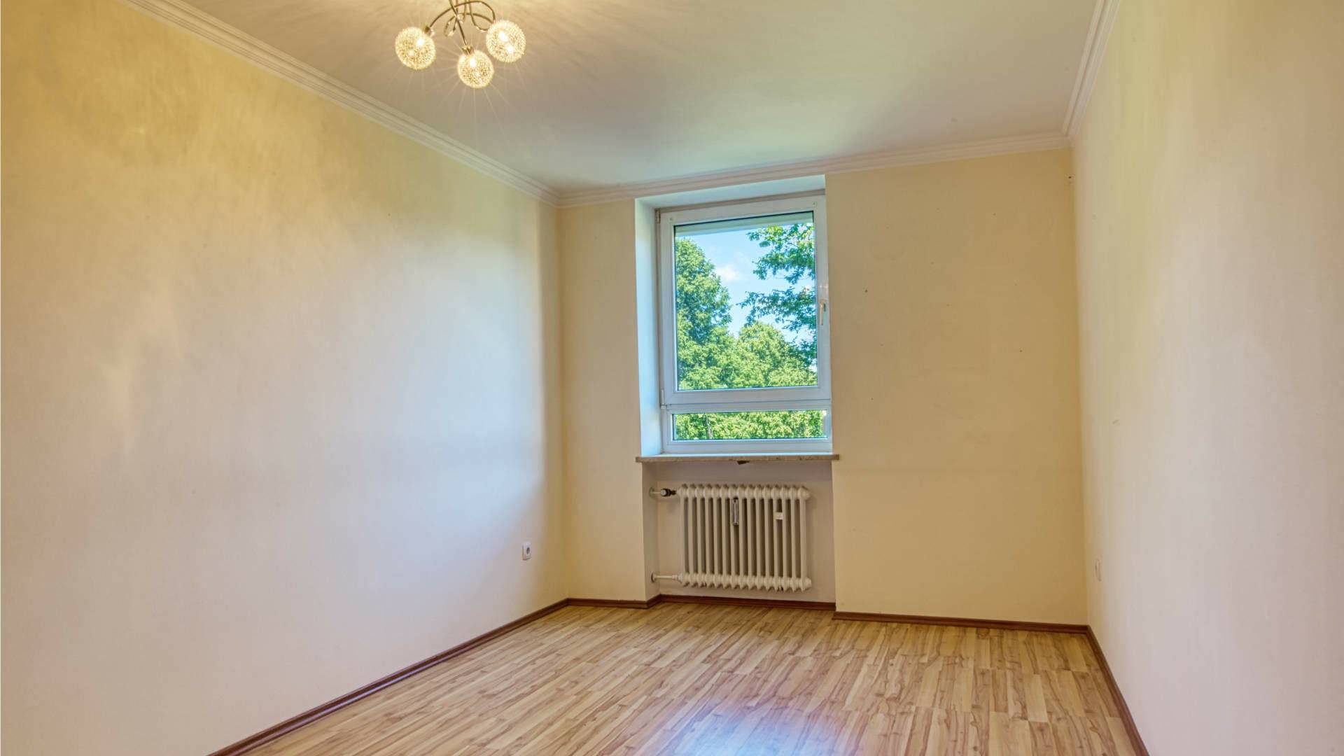 Empty room in the apartment in Aubing with a ceiling light, windows, radiators, and a light wooden floor