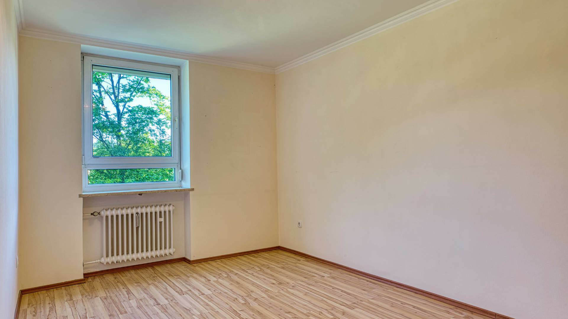Empty room in the apartment in Aubing with bright walls, windows, radiators and wooden laminate floor