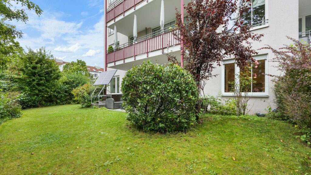 Grüne Gartenfläche mit rotem Herbstbaum und Balkon an Gartenwohnung München-Berg am Laim