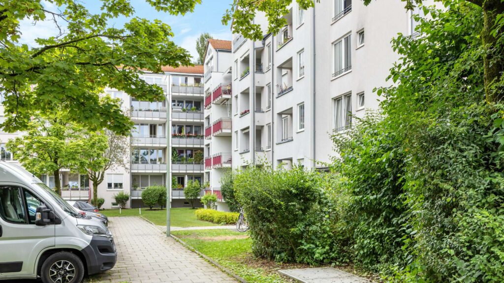Weißes Mehrfamilienhaus mit roten Balkonen und begrüntem Weg in München-Berg am Laim