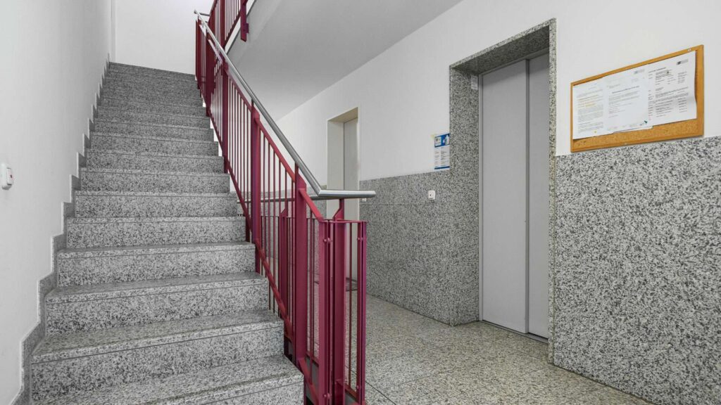 Treppenhaus mit rotem Geländer, Steinstufen und Aufzug in Mehrfamilienhaus München-Berg am Laim