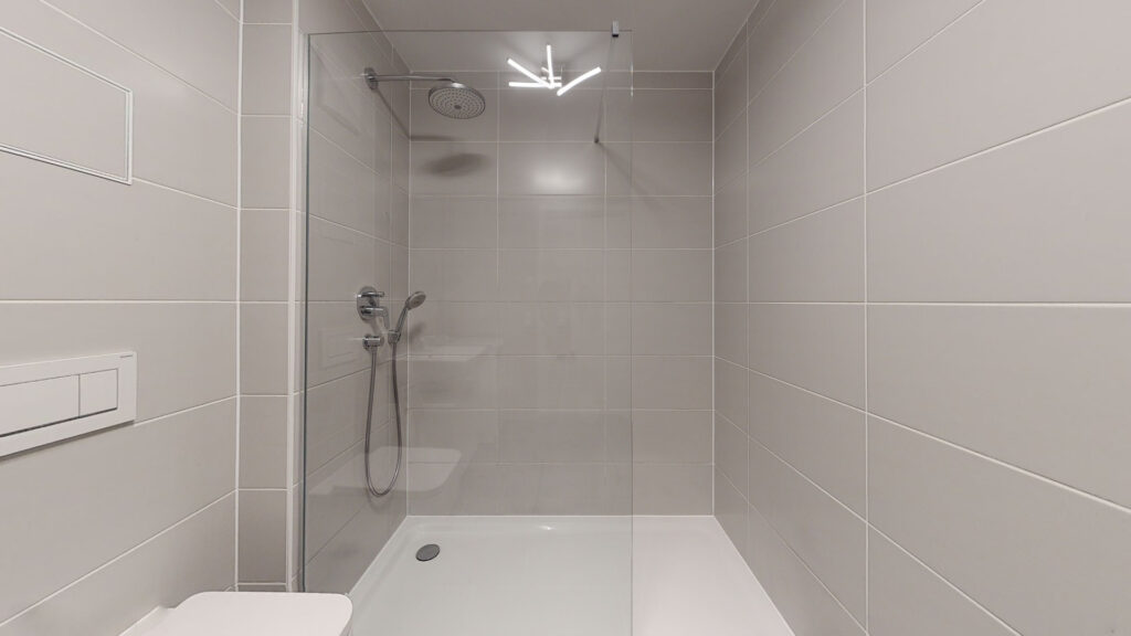 Walk-in shower with rain shower head and light wall tiles in an apartment in Munich's Berg am Laim district