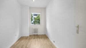 Empty narrow room with window and wooden floor in condominium in Munich Berg am Laim