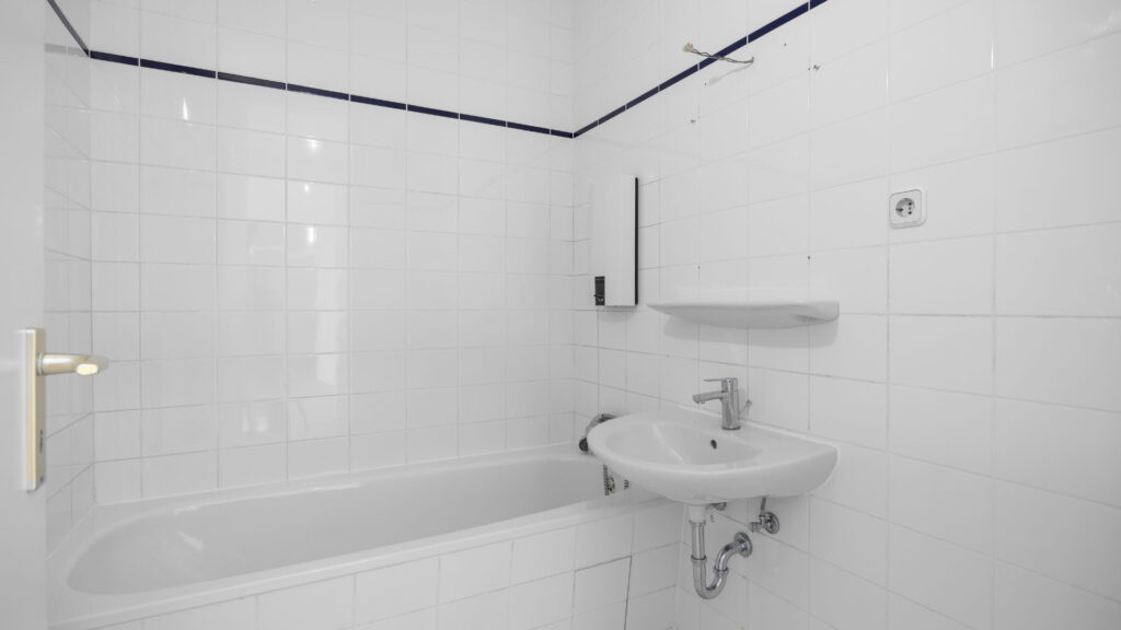Older white-tiled bathroom with tub and sink in Berg am Laim condominium