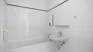 Older white-tiled bathroom with tub and sink in Berg am Laim condominium