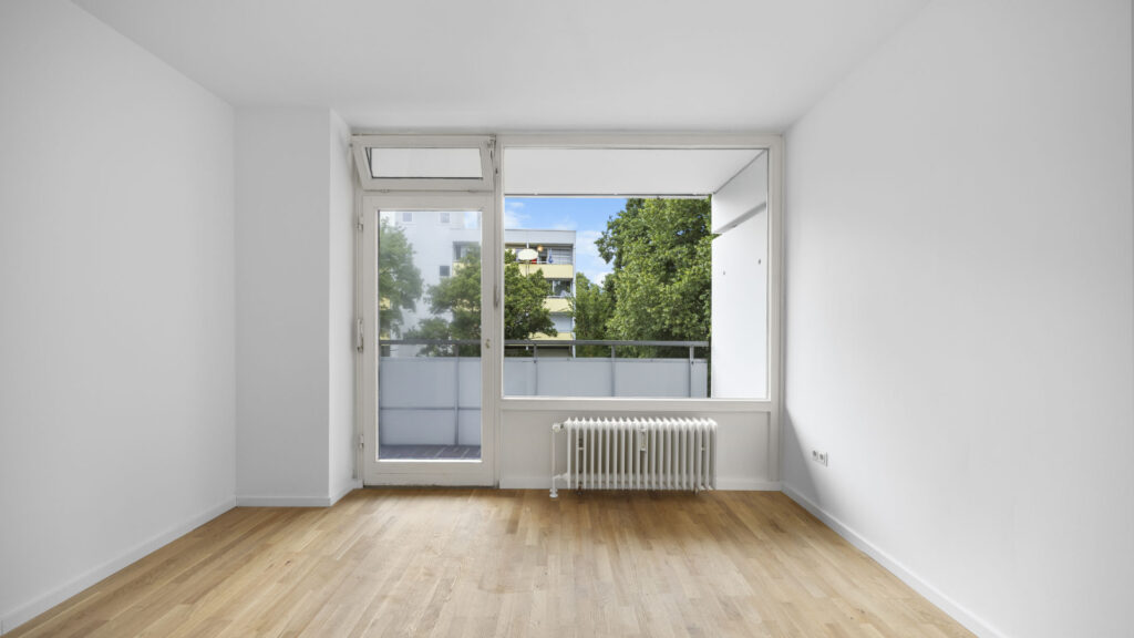 Empty bedroom with floor-to-ceiling windows and a view of neighboring buildings in Berg am Laim