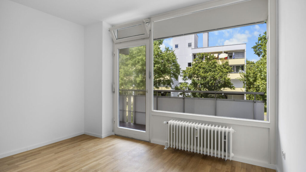 Empty bedroom with balcony door and radiator in condominium in Munich Berg am Laim